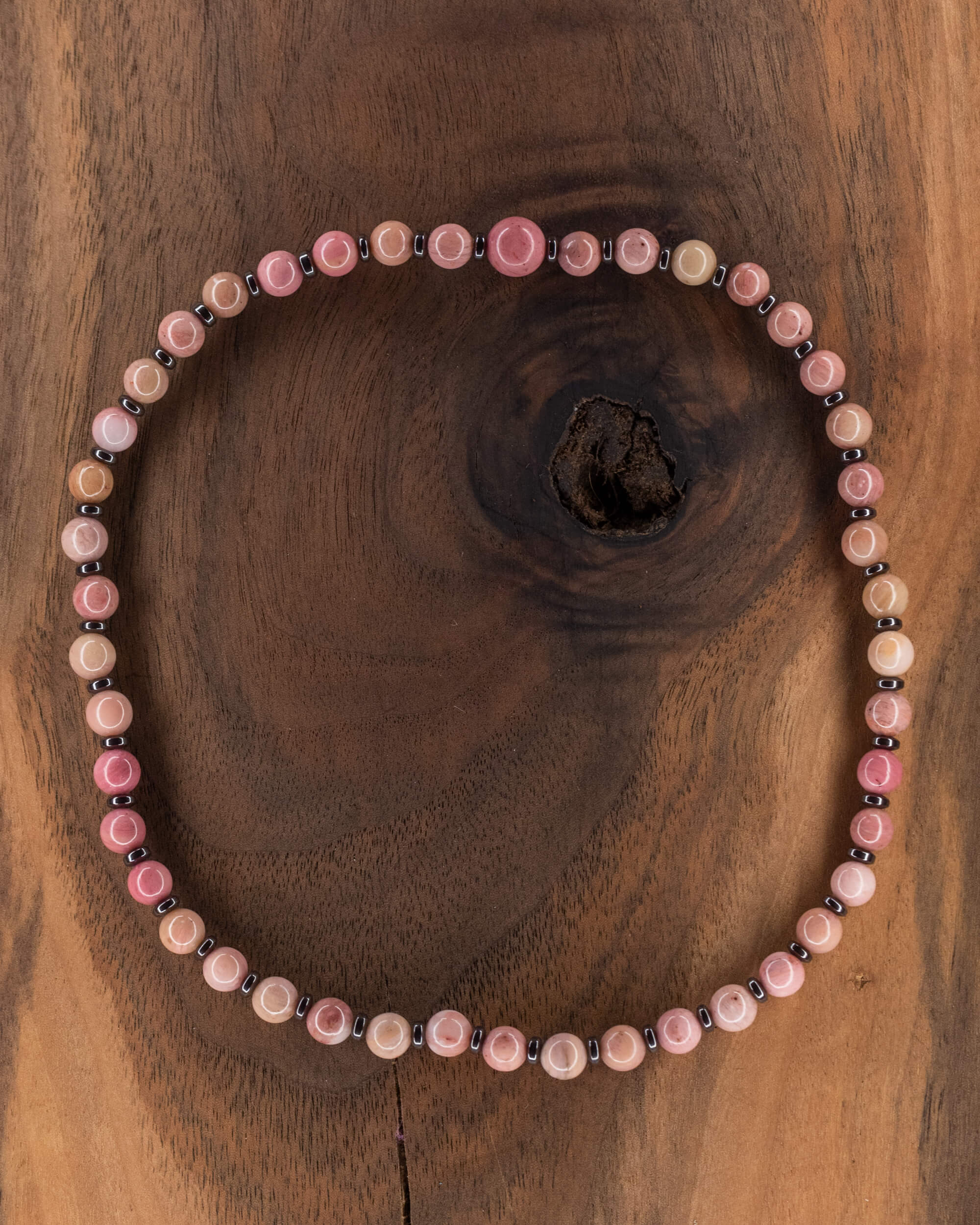 Codificador de Rodonita Rosa y Hematita, pieza completa en círculo sobre madera oscura