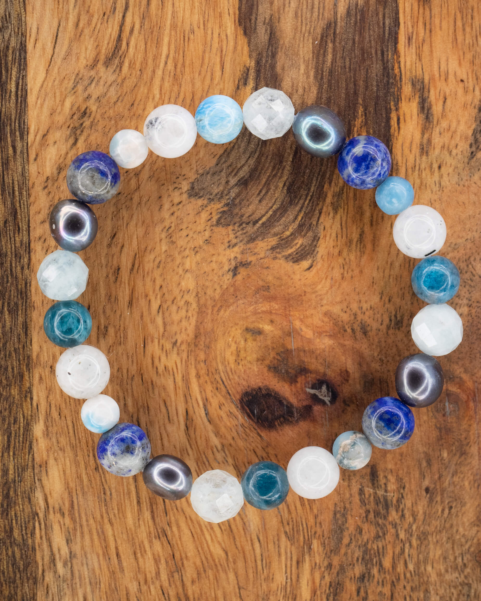 Pulsera mix de Aguamarina, Perla Negra, Lapislázuli, Apatita Azul y Piedra Luna, pieza completa sobre madera