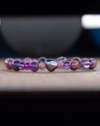 Pulsera de minerales morados en perspectiva lateral, fondo desenfocado con tazón