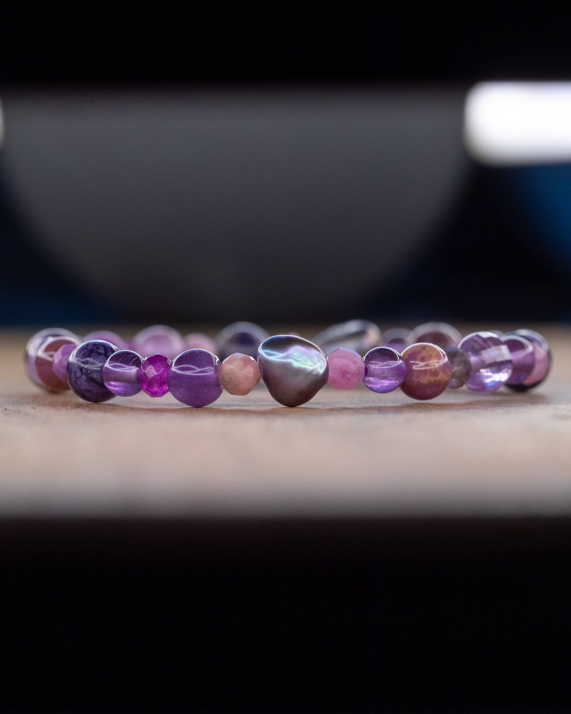 Pulsera de minerales morados en perspectiva lateral, fondo desenfocado con tazón