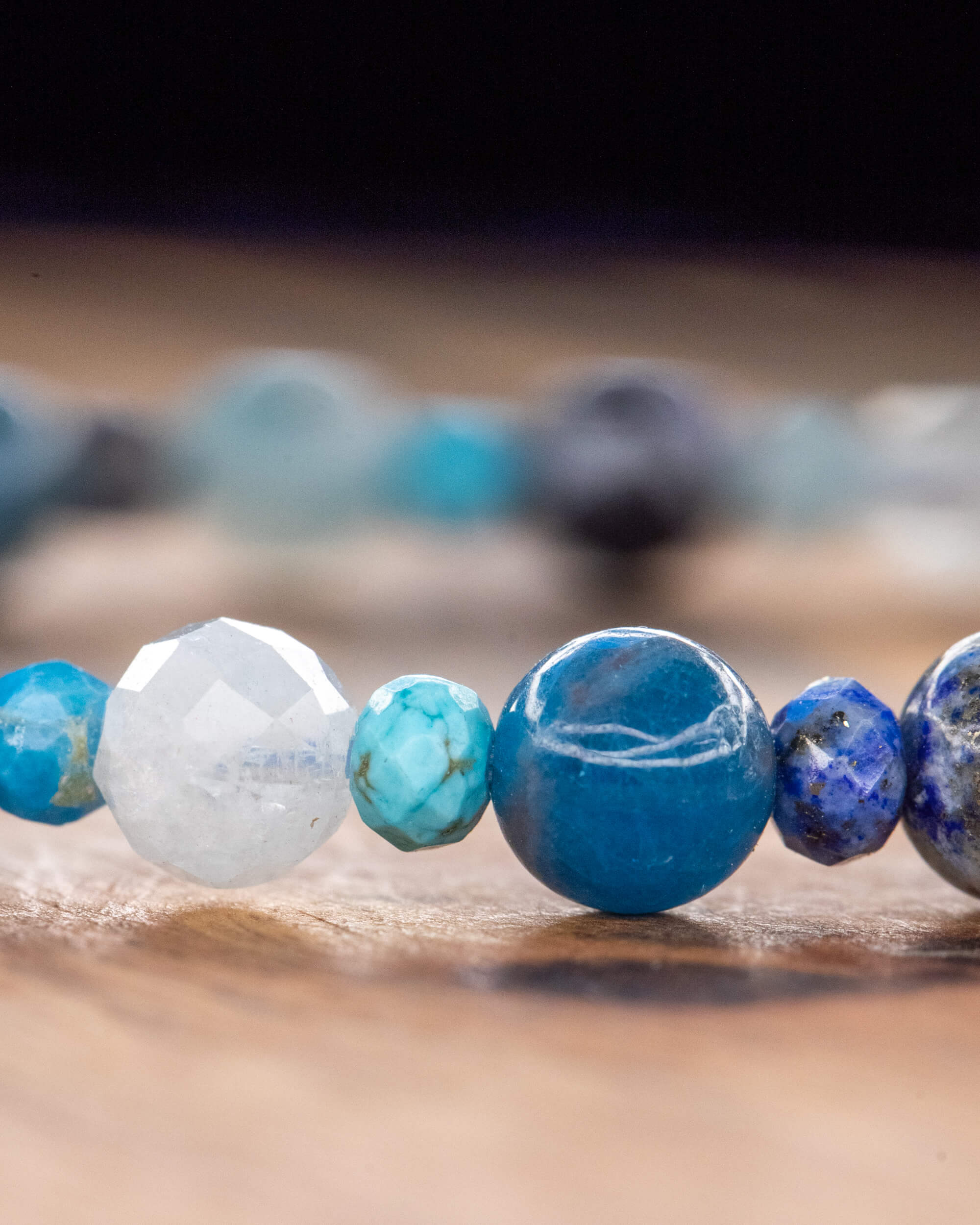 Detalle macro del Mix de Minerales Azules, cuenta blanca facetada junto a cuentas turquesa y azul sobre madera